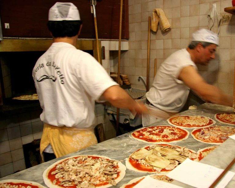 Pizzaioli preparing Roman pizzas at the marble counter inside Pizzeria Da Baffetto in Rome